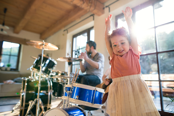 Portrait of happy small children with father indoors at home, playing drums.