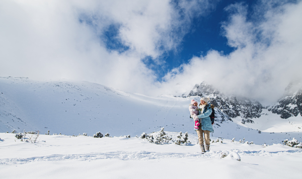 Portrait of mother with happy small daughter standing in winter nature, walking.