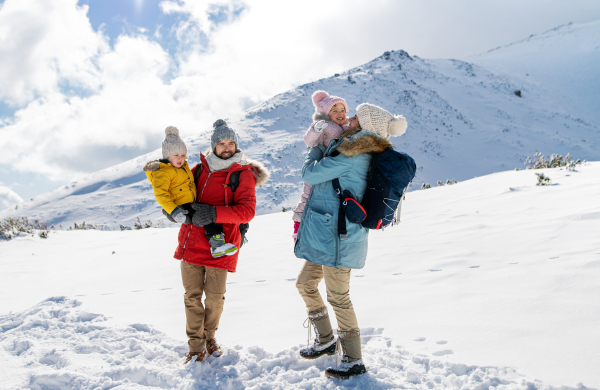 Front view portrait of father and mother with two small children in winter nature, standing in the snow.