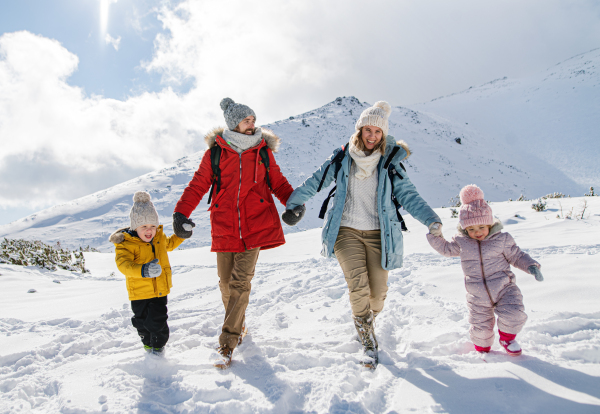 Front view portrait of father and mother with two small children in winter nature, walking in the snow.