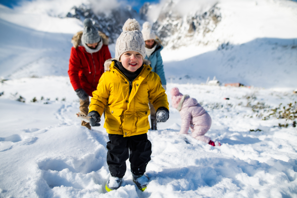 Small boy with family in winter nature, walking in the snow and looking at camera.