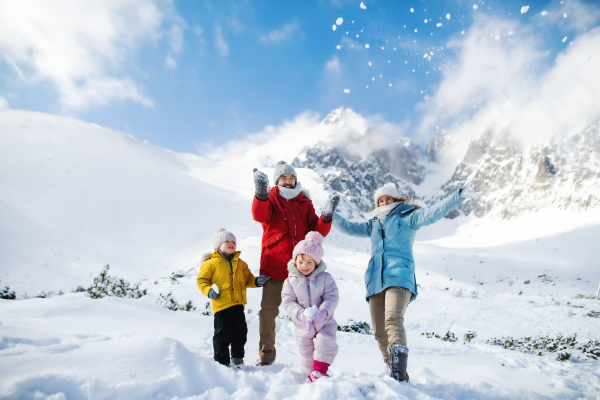 Front view portrait of father and mother with two small children in winter nature, playing in the snow.