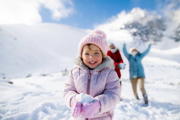 Portrait of cheerful small girl playing in snow in winter nature, playing and looking at camera.