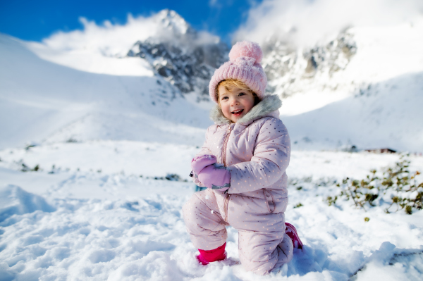 Portrait of cheerful small girl lying in snow in winter nature, playing and looking at camera.