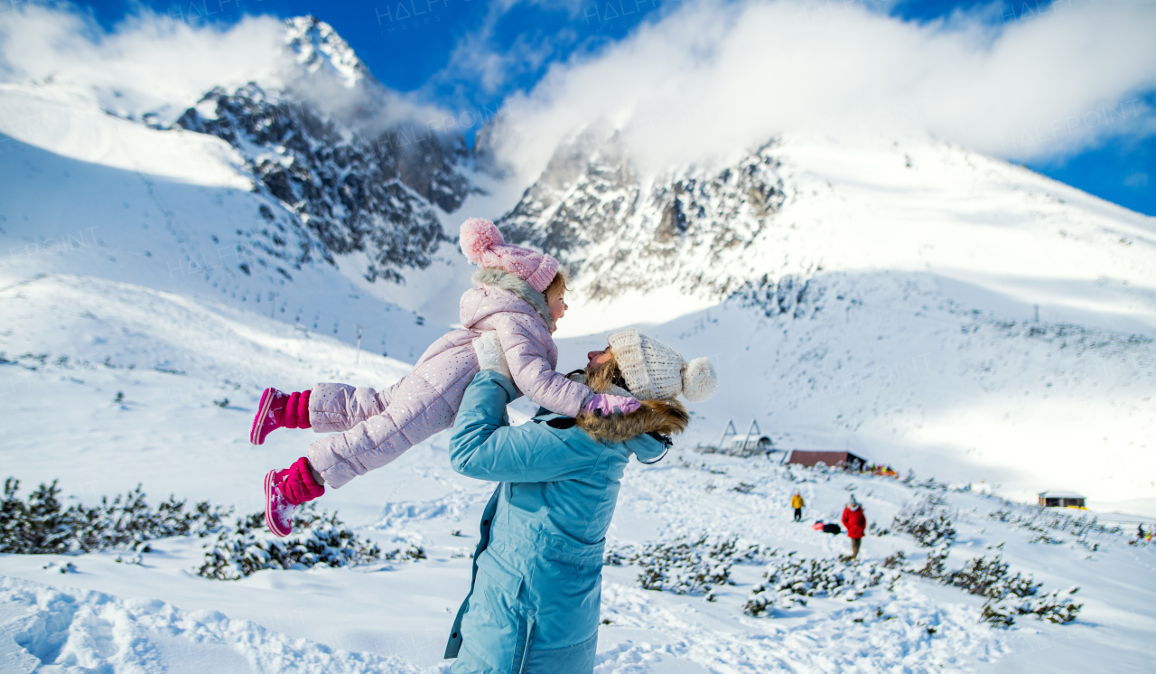 Portrait of mother with happy small daughter standing in winter nature, having fun.