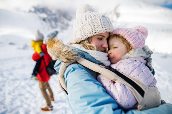 Portrait of mother with happy small daughter in carrier standing in winter nature, resting.