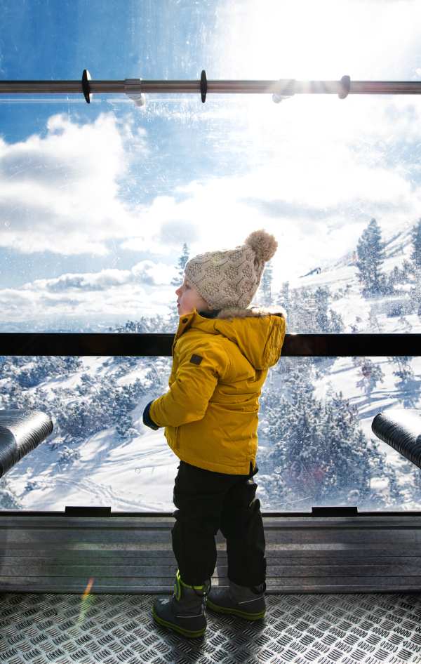 A rear view of small child inside a cable car cabin, holiday in snowy winter nature.