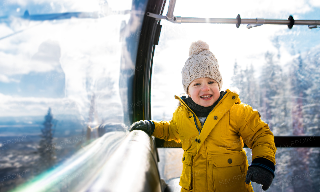 Front view of small child inside a cable car cabin, holiday in snowy winter nature, looking at camera.