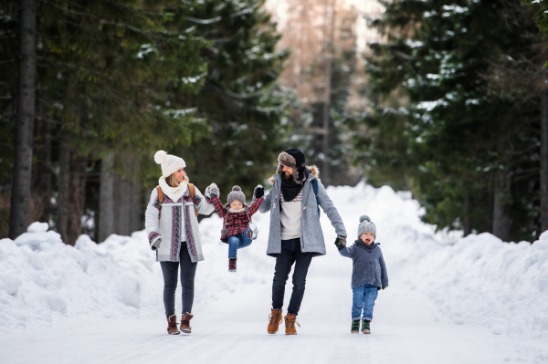 Front view portrait of father and mother with two small children in winter nature, walking in the snow.