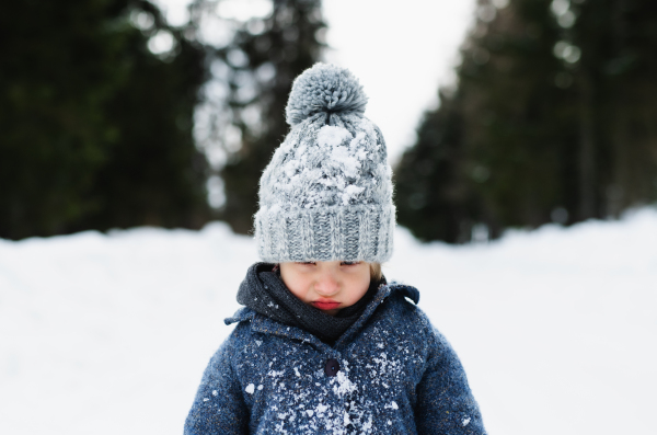 Front view of unhappy and sad small child standing in snow, holiday in winter nature.