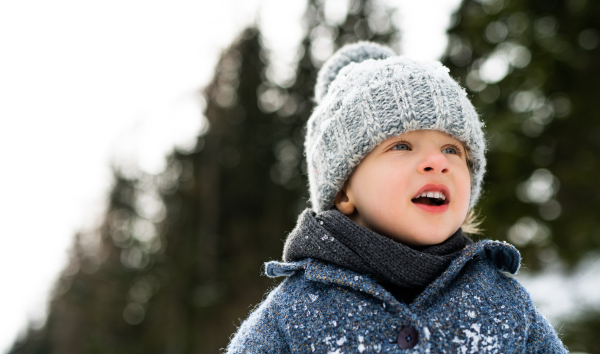 Front view of happy small child standing in snow, holiday in winter nature.