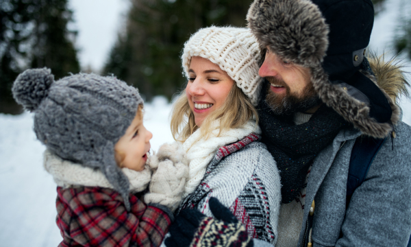 Side view of father and mother with small child in winter nature, standing in the snow.