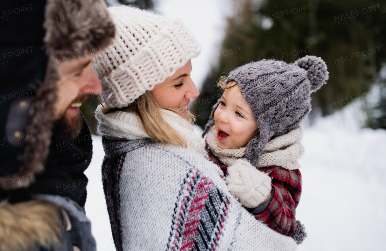 Side view of father and mother with small child in winter nature, standing in the snow.