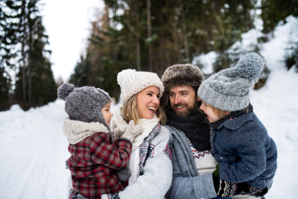 Front view portrait of father and mother with two small children in winter nature, standing in the snow.