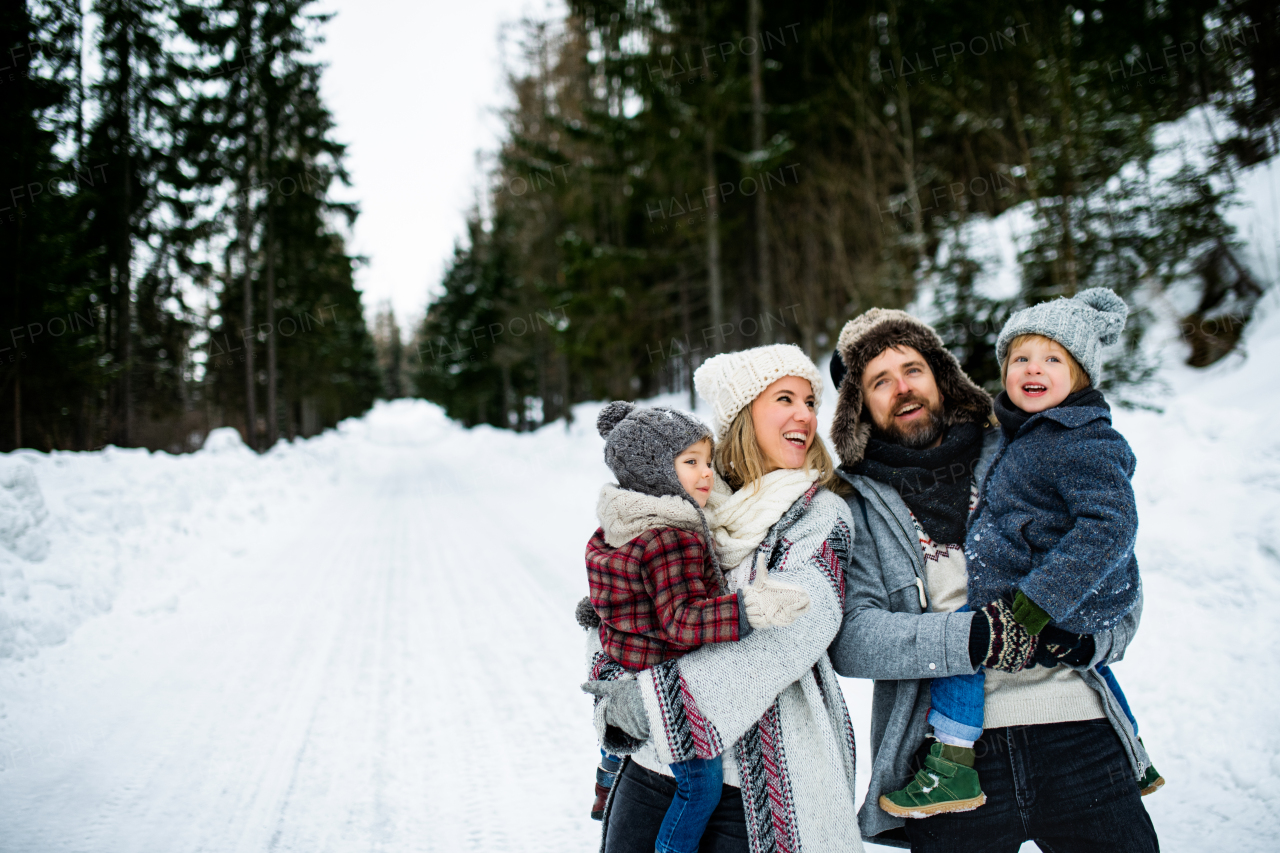 Side view portrait of father and mother with two small children in winter nature, standing in the snow.