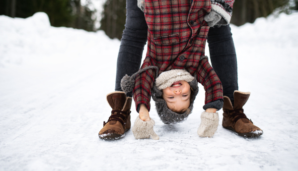 Midsection of unrecognizable mother holding small daughter upside down in winter nature.