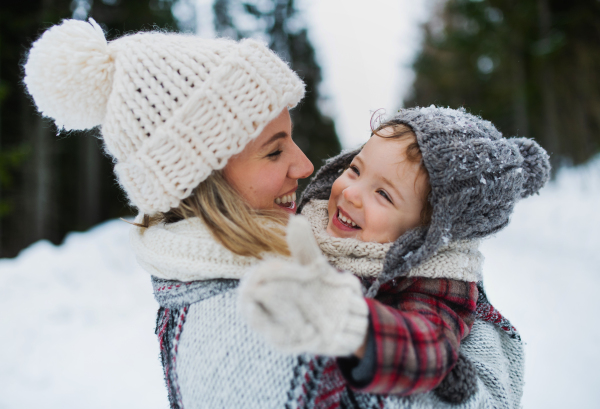 Side view of cheerful mother with small daughter standing in winter nature, laughing.