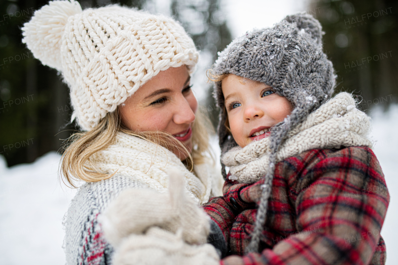 Side view of cheerful mother with small daughter standing in winter nature, laughing.