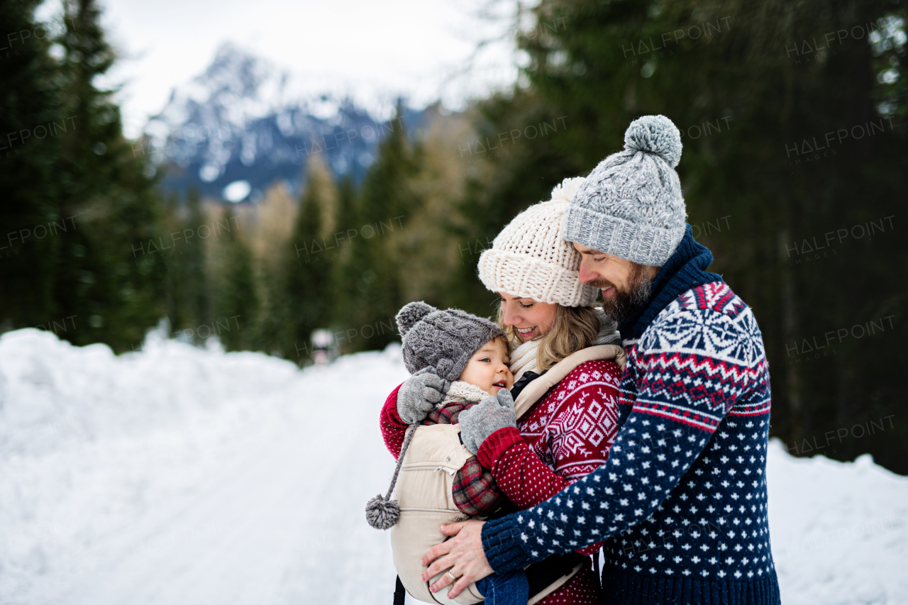 Side view of father and mother with small child in winter nature, standing in the snow.