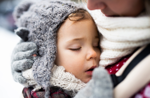 Close-up of sleeping small daughter in carrier and unrecognizable mother in winter nature.