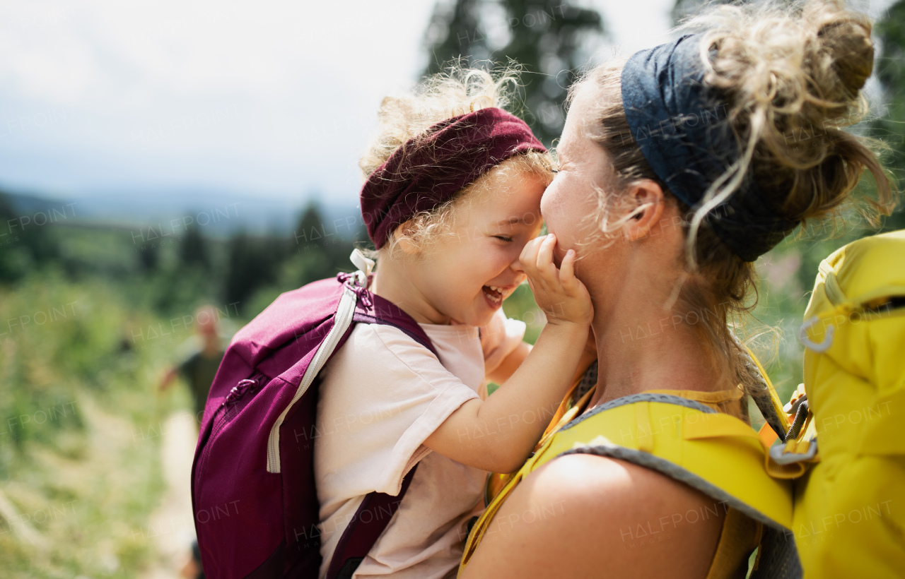 Cheerful mother with small daughter hiking outdoors in summer nature, cuddling.