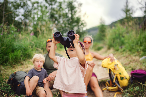 Front view of family with small children hiking outdoors in summer nature, sitting and resting.