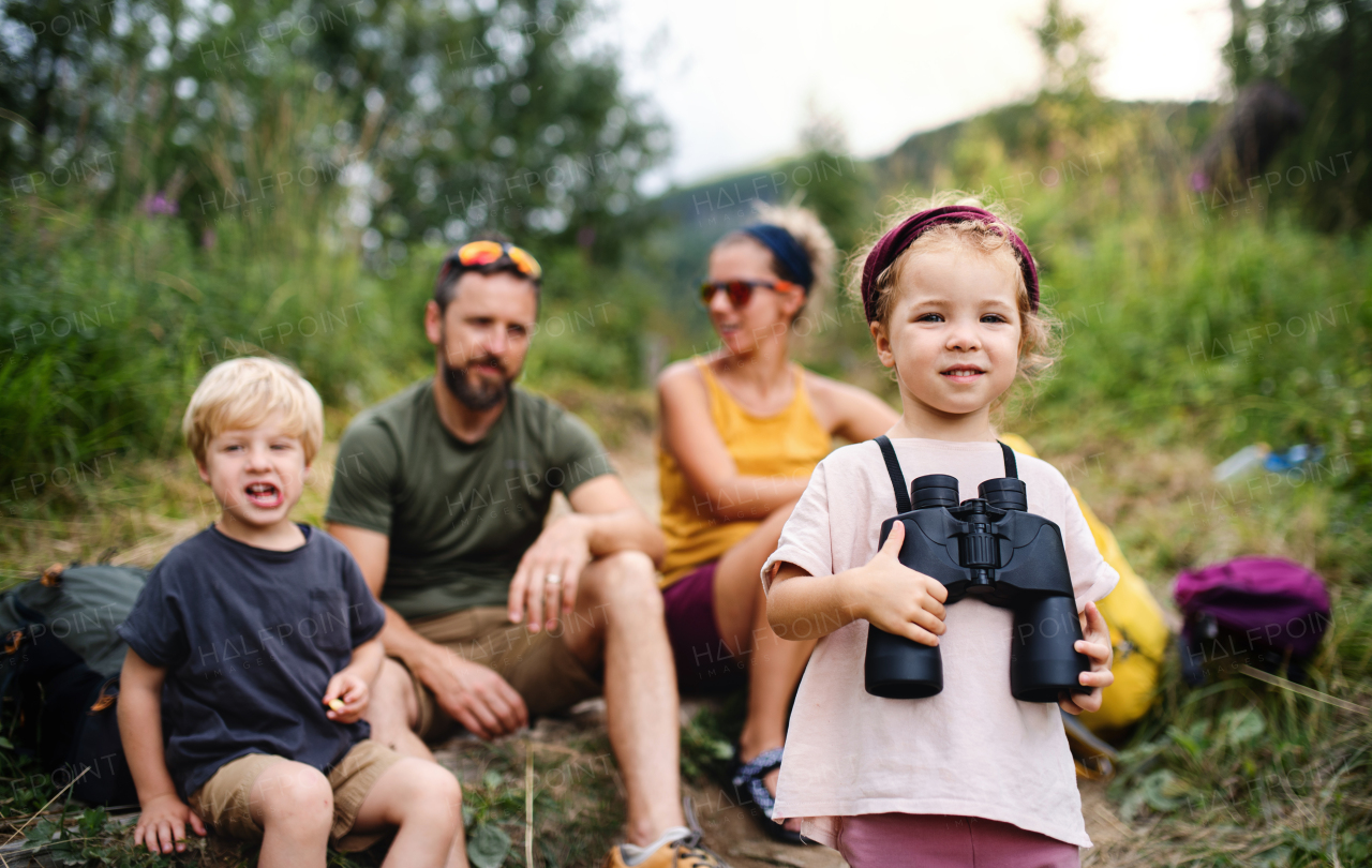 Front view of family with small children hiking outdoors in summer nature, sitting and resting.