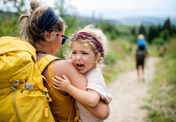 Rear view of mother with small crying toddler daughter hiking outdoors in summer nature.