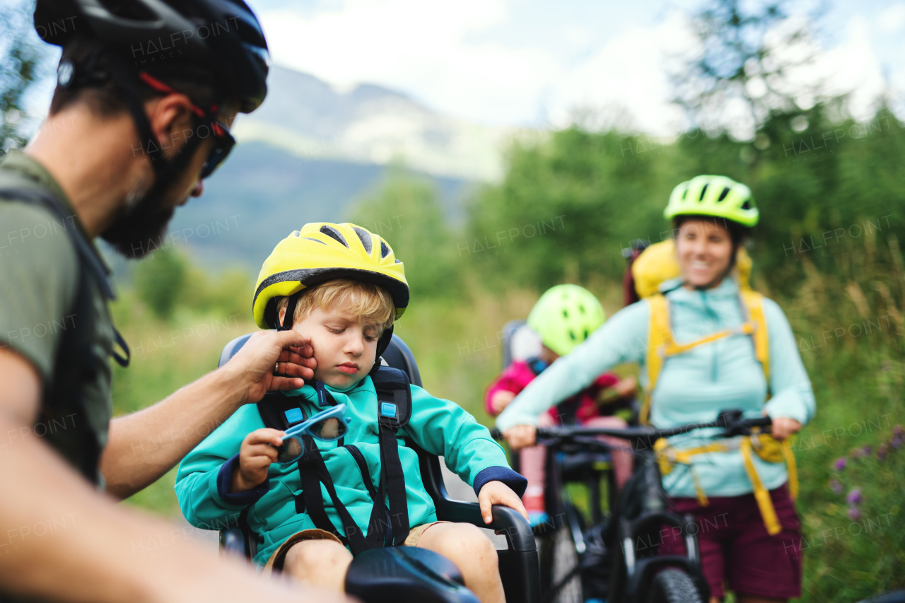 Tired family with small children cycling outdoors in summer nature.