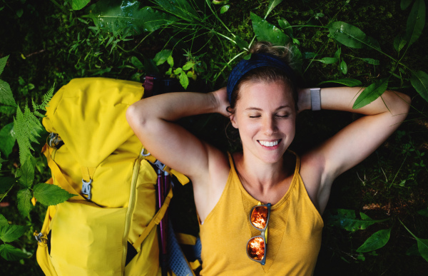 Top view of happy woman hiker lying on the ground outdoors in forest, resting.