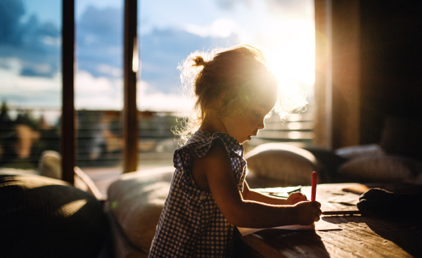 Portrait of small girl drawing pictures in wooden cabin, holiday in nature concept.