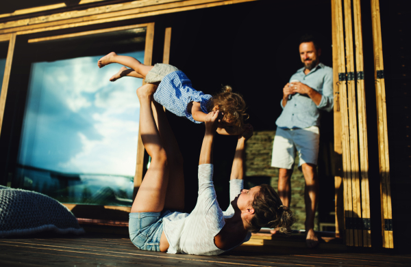 Happy family with small daughter having fun on patio of wooden cabin, holiday in nature concept.