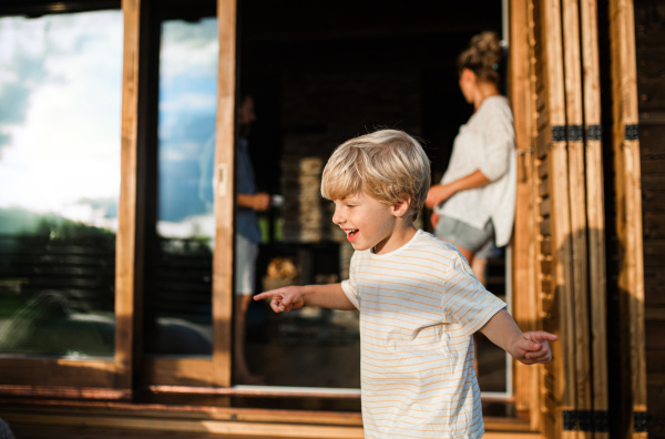 Cheerful small boy with parents on patio of wooden cabin, holiday in nature concept.