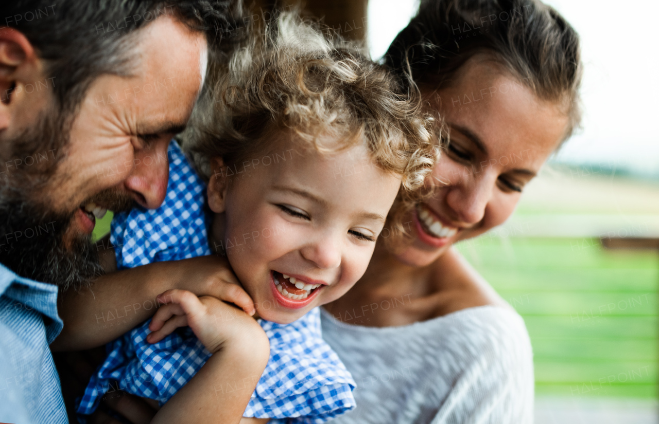 Close-up portrait of happy family with small daughter by wooden cabin, holiday in nature concept.