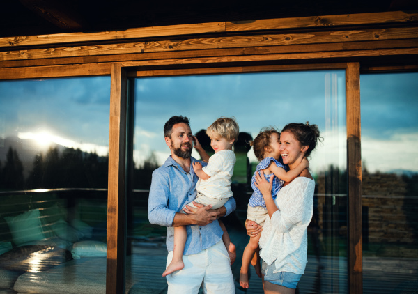 Happy family with small children standing on patio by wooden cabin, holiday in nature concept.