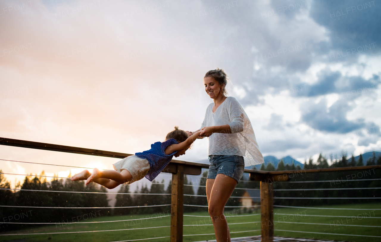 Happy mother with small daughter playing on patio of wooden cabin, holiday in nature concept.