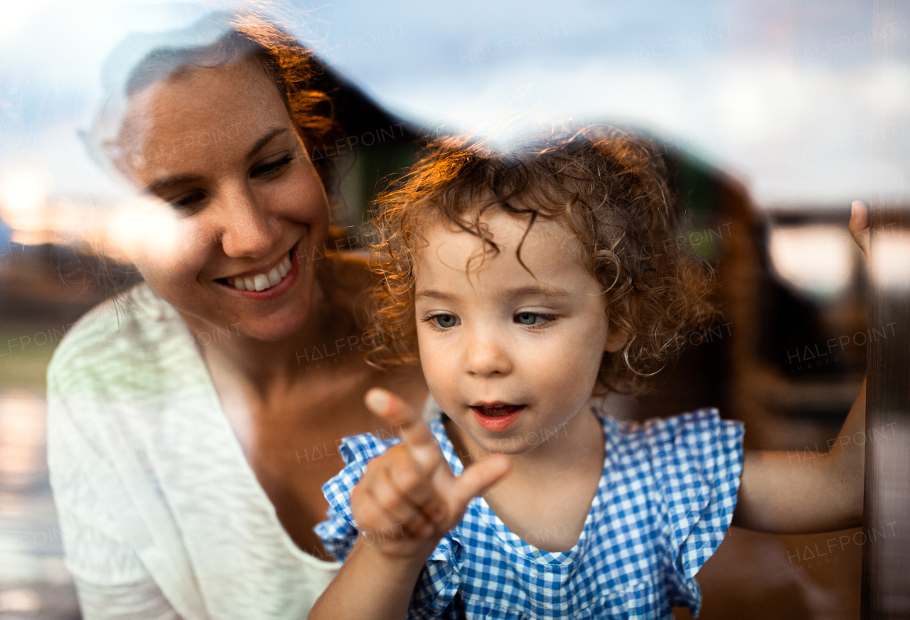 Portrait of small girl with mother by window, holiday in nature concept. Shot through glass.