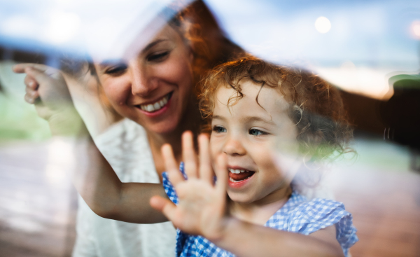 Portrait of small girl with mother by window, holiday in nature concept. Shot through glass.