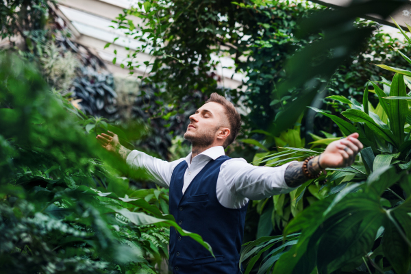 Young man standing in botanical garden, arms stretched. Green bussiness concept.