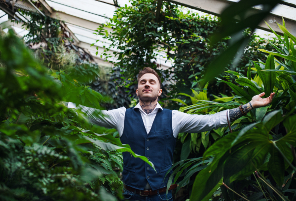 Young man standing in botanical garden, arms stretched. Green bussiness concept.