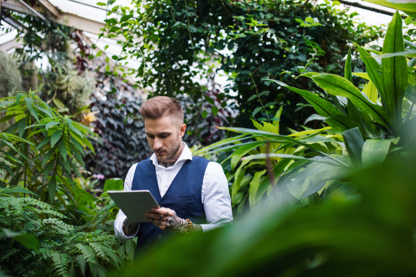 Young man with tablet standing in botanical garden, working. Green bussiness concept.