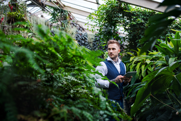 Young man with tablet standing in botanical garden, working. Green bussiness concept.