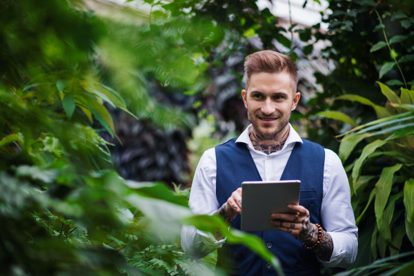 Young man with tablet standing in botanical garden, working. Green bussiness concept.