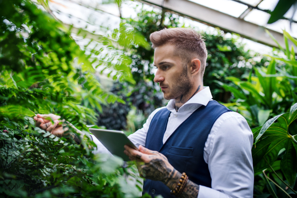 Young man with tablet standing in botanical garden, working. Green bussiness concept.