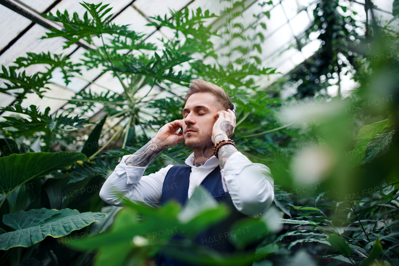 Young man with headphones standing in botanical garden, listening to music. Green bussiness concept.