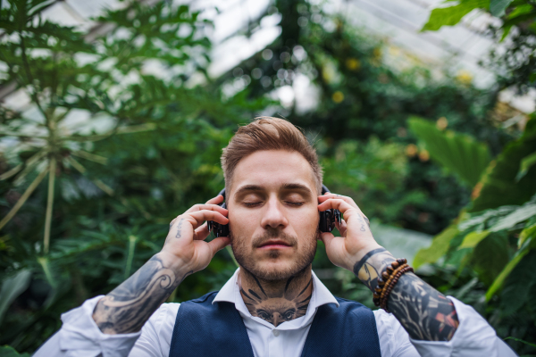 Young man with headphones standing in greenhouse in botanical garden. Green bussiness concept.