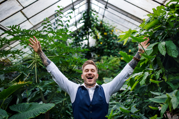 Cheerful young man standing in botanical garden, arms stretched. Green bussiness concept.