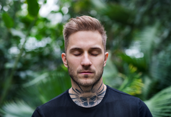 A front view of young man with closed eyes standing in botanical garden.