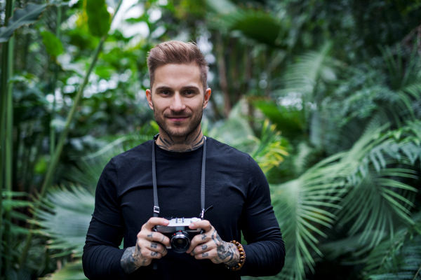 A front view of young man with camera standing in botanical garden.