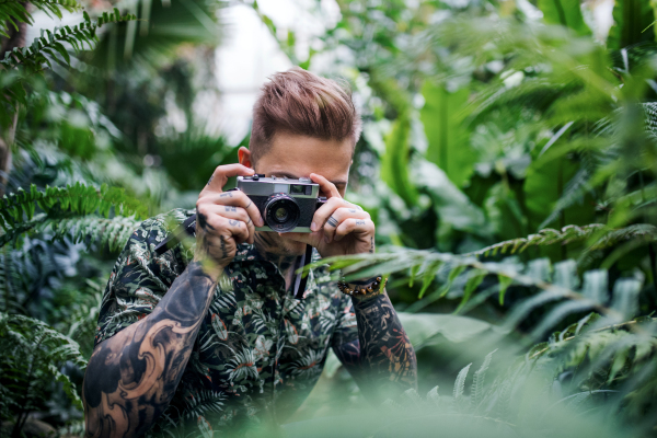 A young man with camera standing in botanical garden, taking photographs.